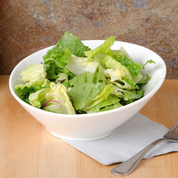 A CAC bone white porcelain salad bowl filled with lettuce on a napkin.