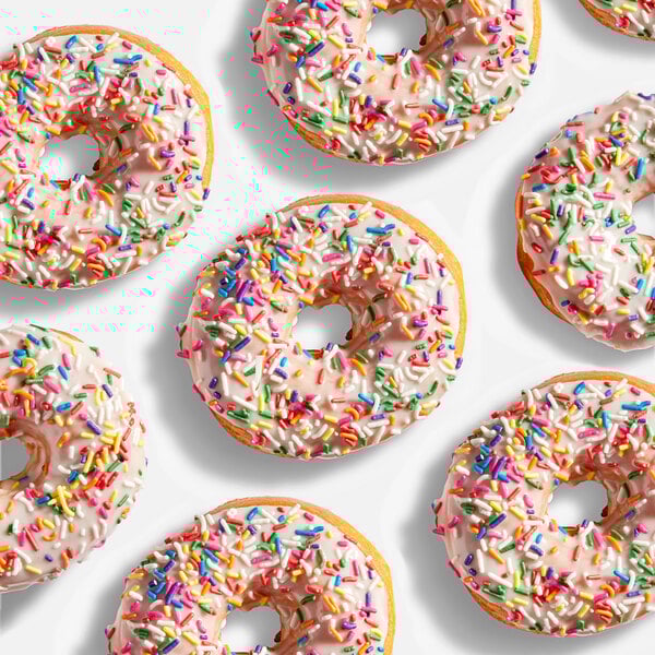 A group of donuts with white icing and colorful rainbow sprinkles.