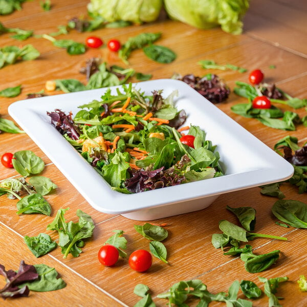 A salad in a white bowl on a wooden surface.