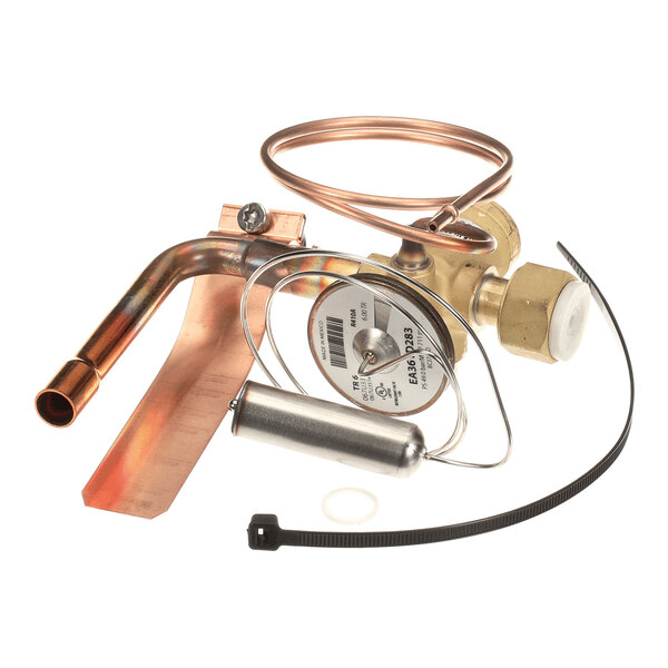 A metal valve assembly with copper tubing, a cylindrical component, and a black zip tie, likely part of a refrigeration or HVAC system.