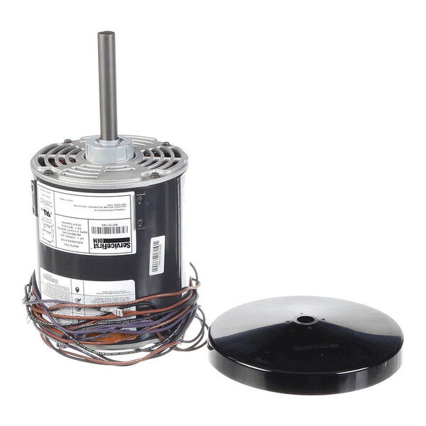 A cylindrical electric motor with a protruding shaft, attached wires, and a separate round black cover placed beside it.