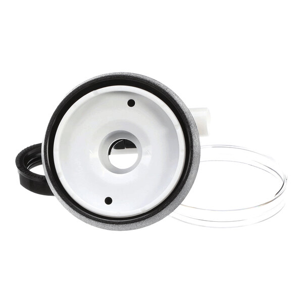 A round, white and black plastic component with a central hole, two smaller holes, and an attached clear tube, viewed from the front.