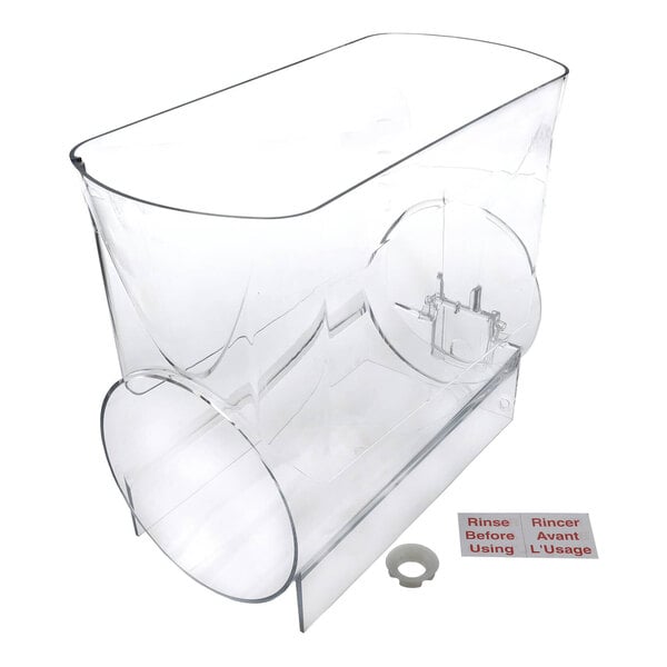 A clear, rectangular plastic container with rounded edges, a circular opening on one side, and two small labels and a white ring placed beside it.