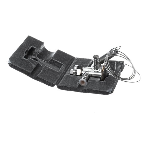 A metal valve with attached tubing is placed in a custom black foam packaging insert.
