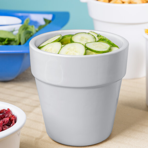 A Tablecraft natural cast aluminum round condiment bowl filled with cucumbers on a table with bowls of cucumbers and other food.