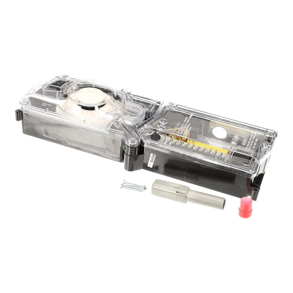 A rectangular device with a transparent cover, internal components visible, and several small accessories including a screw, a gray connector, and a red cap placed in front of it.