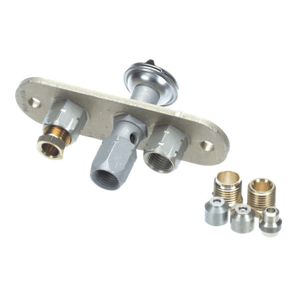 A metal pilot burner assembly with multiple threaded ports and a set of small brass and steel fittings placed beside it.