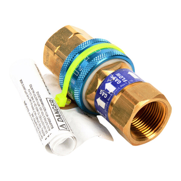 A brass and blue metal gas quick disconnect fitting with a yellow plastic tag and a rolled-up warning label attached.