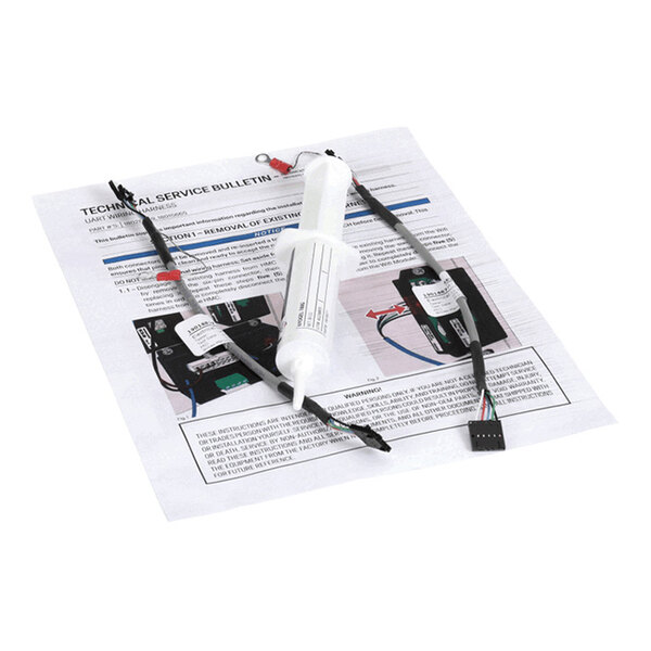A white syringe-like tool and a cable with connectors are placed on top of a printed technical service bulletin with images and instructions.