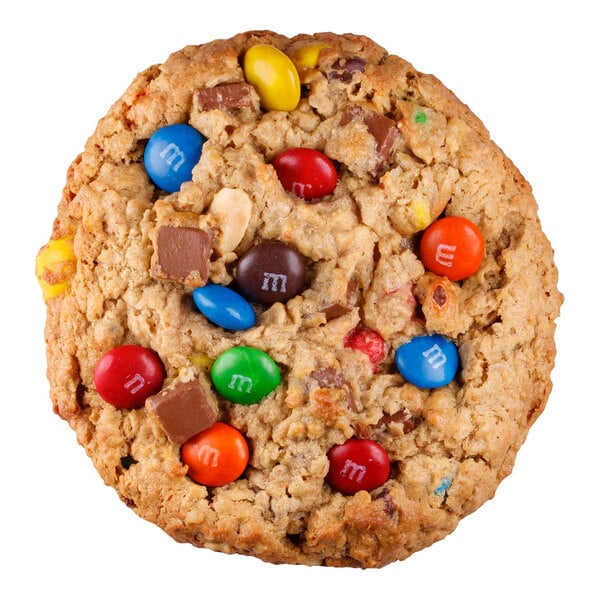 A large cookie with a rough texture, containing colorful candy-coated chocolates, chocolate chunks, and visible peanuts.