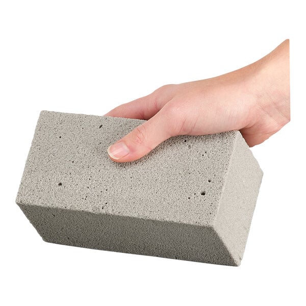 A hand holding a rectangular, gray, porous abrasive stone.
