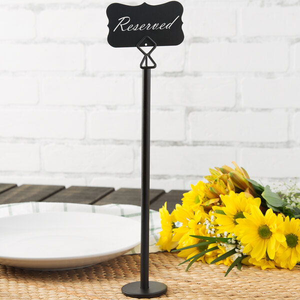 A tall black metal card holder with a sign reading 'Reserved' is placed on a table next to a white plate and a bouquet of yellow flowers.