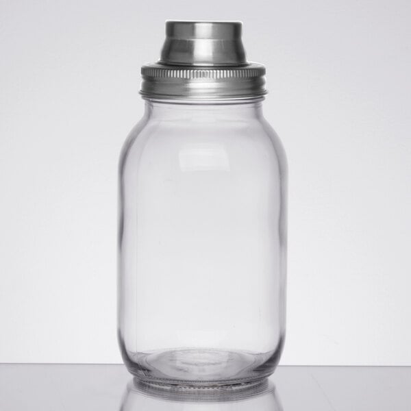 A clear glass jar with a metal screw-on lid and a metal cap on top, resembling a mason jar cocktail shaker.