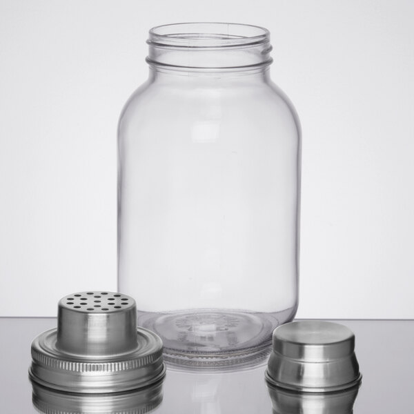 A clear glass jar with a metal strainer lid and a metal cap, all separated and displayed on a reflective surface.