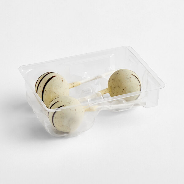 Three white chocolate-coated cake pops with dark chocolate drizzle are placed in a clear plastic tray.