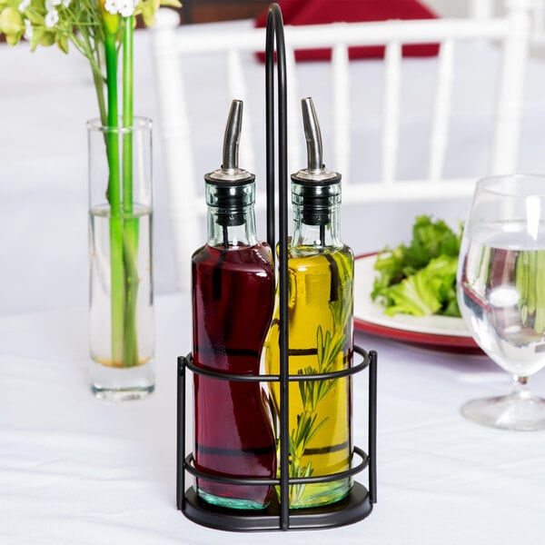 Two glass bottles, one filled with red liquid and the other with yellow liquid and herbs, are held in a black metal rack on a white tablecloth.