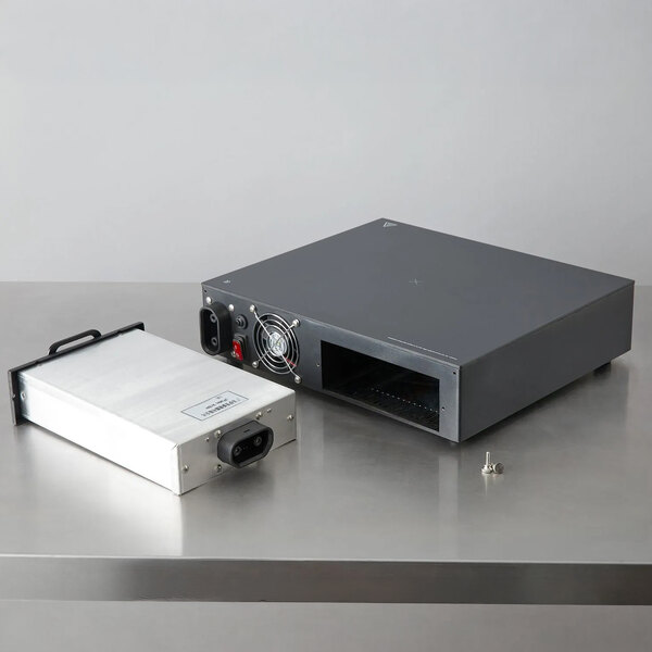 A rectangular metal induction warmer with a removable battery pack and a few screws, placed on a stainless steel surface.