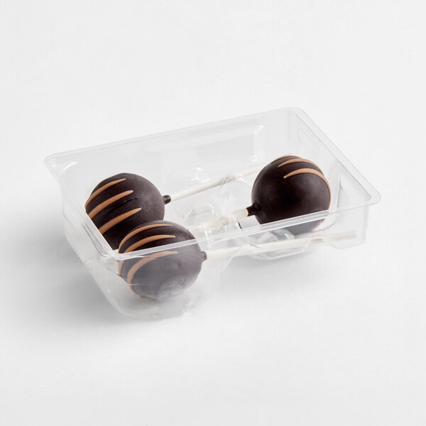 Three chocolate-covered cake pops with light brown drizzle are placed in a clear plastic tray.