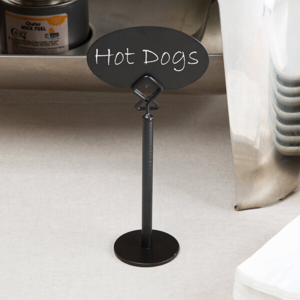 A black metal card holder with an oval sign displaying the words 'Hot Dogs' written in white.