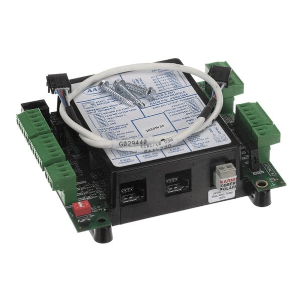 An electronic circuit board with green terminal blocks, a white cable, screws, and a label on top.