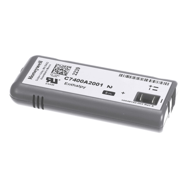 A rectangular electronic sensor module with a white label displaying text, barcodes, and a small window on one end.