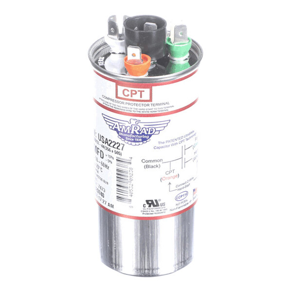 A cylindrical metallic capacitor with three color-coded terminals (black, orange, and green) and a label indicating specifications and wiring diagram.