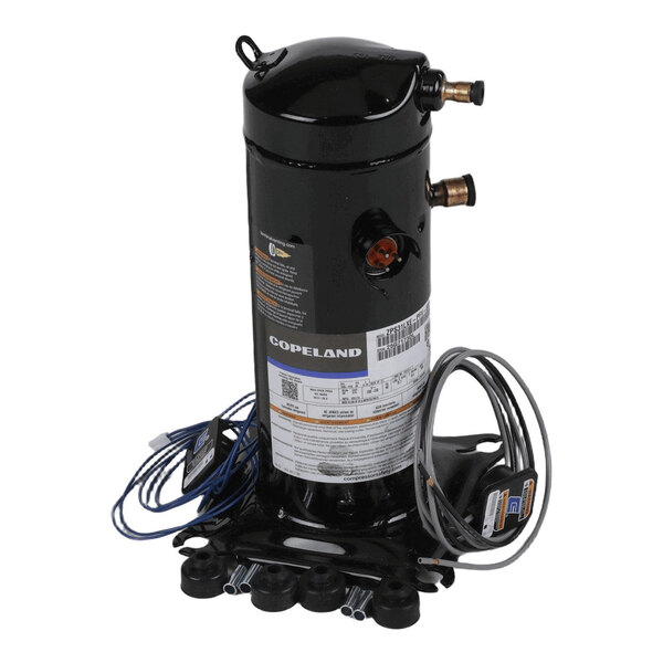 A cylindrical black metal component with attached wires, copper pipe fittings, and a label, mounted on a base.