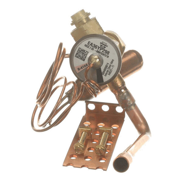 A copper and brass mechanical component with coiled tubing, a round labeled part, and a perforated mounting bracket with two bolts.