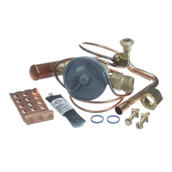 A collection of metal and copper components, including a valve, tubing, fittings, bolts, washers, a copper plate with holes, and a small tube of lubricant or sealant, arranged on a white background.