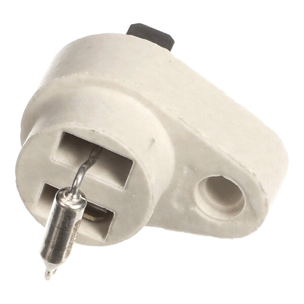 A white, L-shaped ceramic component with two rectangular slots and a cylindrical metal fuse attached to one slot.