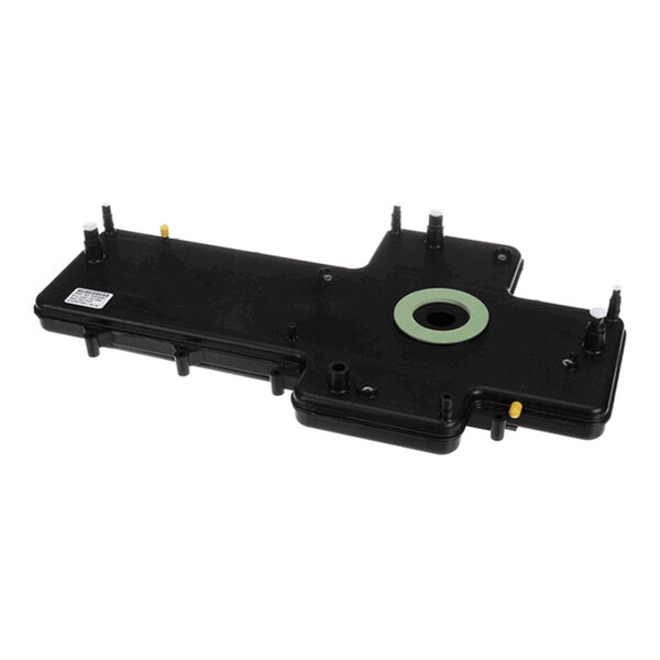 A black, rectangular plastic component with multiple protruding pegs and a central circular opening with a green ring.