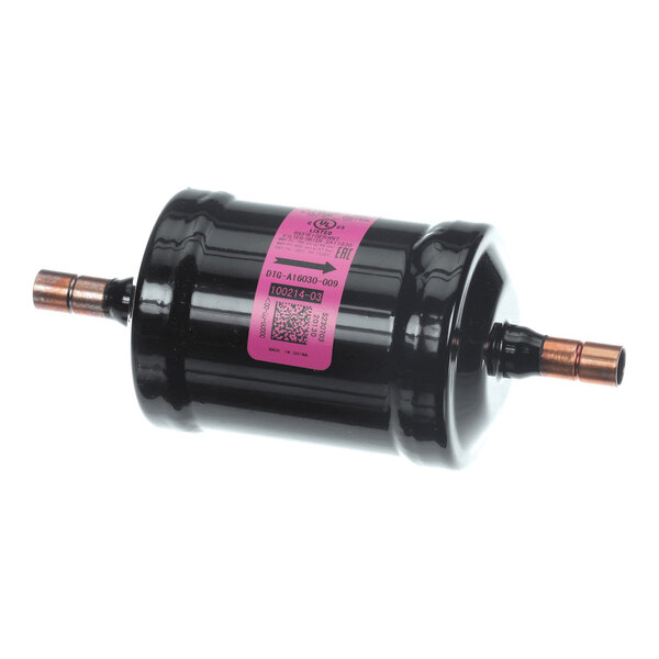 A cylindrical black metal component with copper pipe fittings on both ends and a pink label in the center.