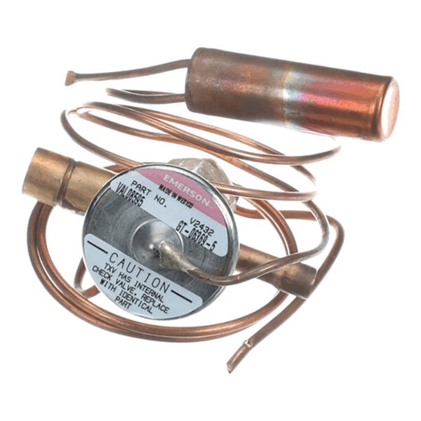 A coiled copper tube assembly with a cylindrical component and a round metal label featuring caution and part information.