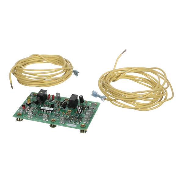 A green electronic circuit board with various components and two coiled yellow wires placed beside it.