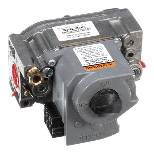 A metallic and plastic mechanical valve component with a large black control knob, various connectors, and warning labels.