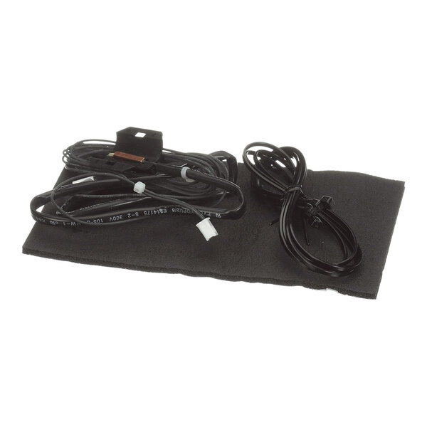 A black mat with two coiled black cables and a small electronic component placed on top.