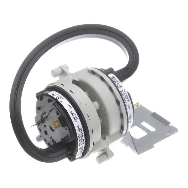 A round mechanical component with a black flexible tube attached, metal mounting bracket, and labeled stickers, likely part of an HVAC system.