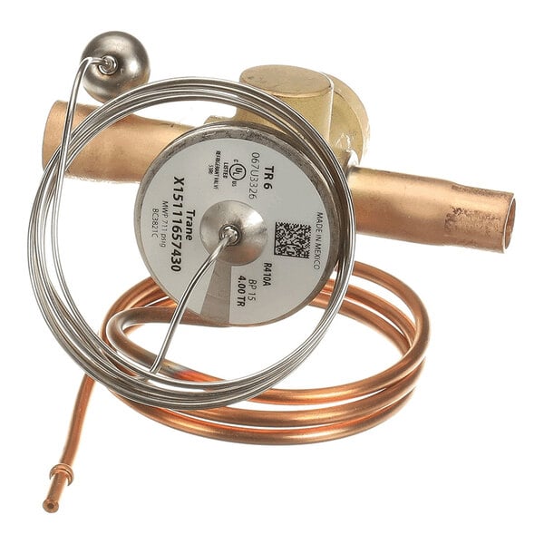 A metallic valve with copper tubing and a coiled capillary tube attached, featuring a round label with technical information.