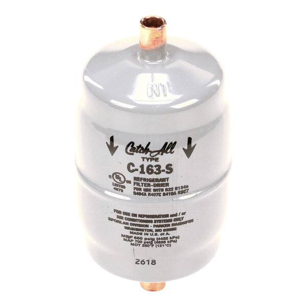 A cylindrical metallic filter-drier with copper inlet and outlet tubes, labeled with specifications and directional arrows.