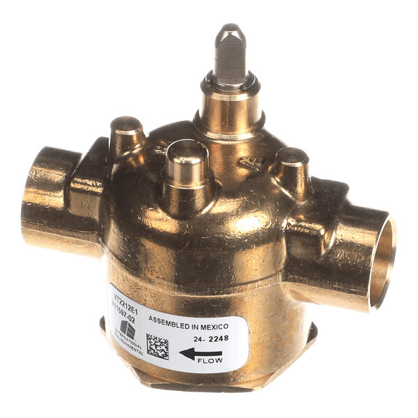 A brass valve with multiple ports and a central stem, featuring a label with product information and a flow direction indicator.