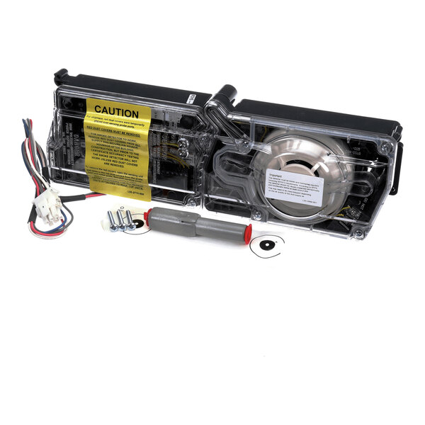A transparent rectangular device with internal components, wiring, screws, and a caution label, accompanied by additional wires and hardware.
