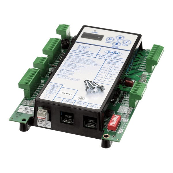An electronic control board with a display panel, multiple green terminal connectors, and several screws placed on top.