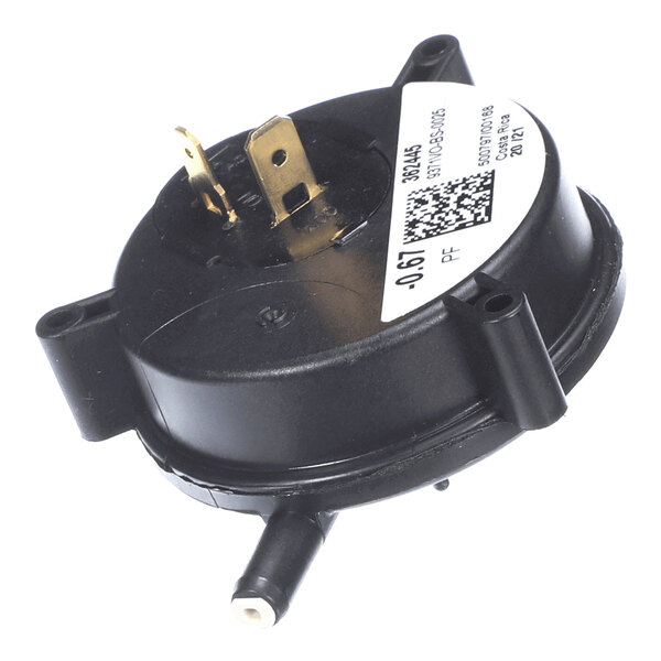 A round black plastic component with two metal prongs, a white label with a QR code, and a protruding nozzle.