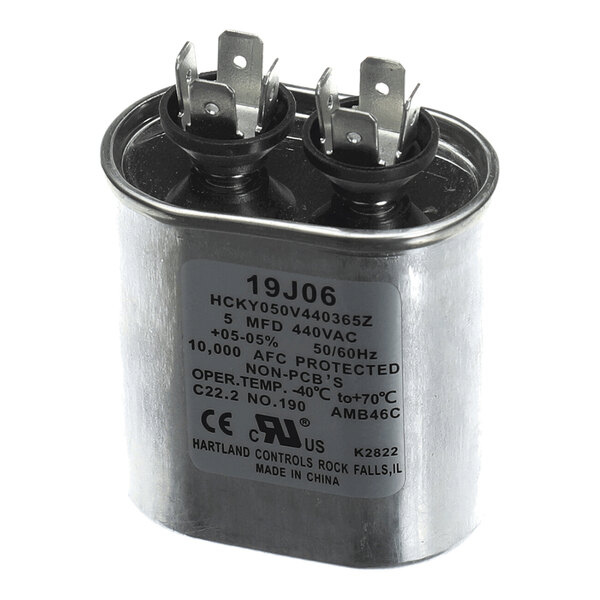 A metallic oval-shaped electrical component with two sets of terminals on top and a label displaying technical specifications.