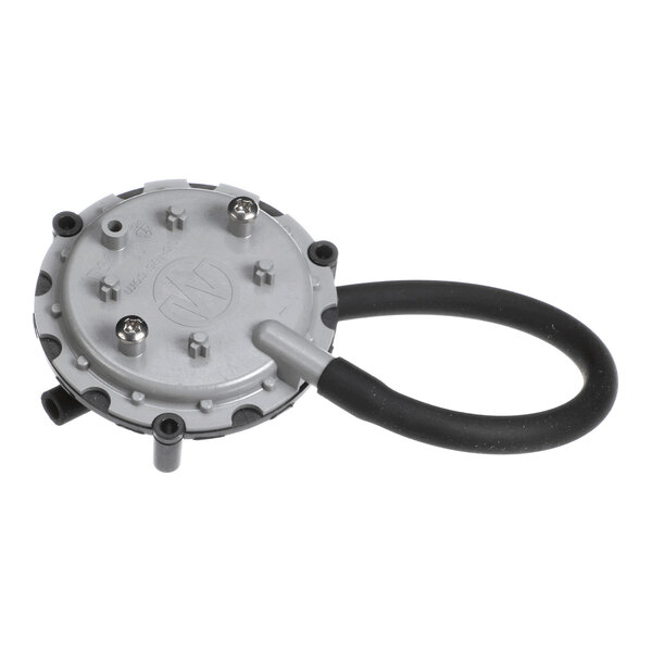 A round, metallic device with multiple screws on top and a black flexible hose attached to one side.