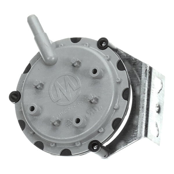 A round, gray mechanical component with a protruding nozzle and multiple small bolts, mounted on a metal bracket.