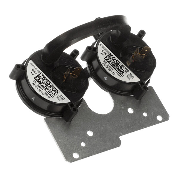 Two round black components with electrical terminals, connected by a black tube, mounted on a metal bracket.