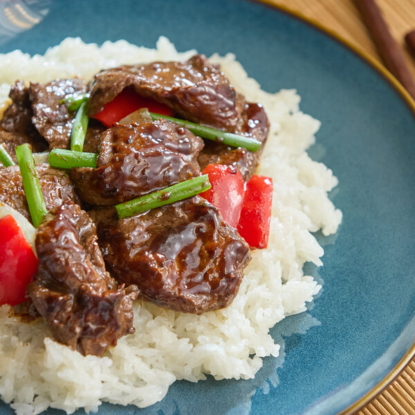 A plate of white rice topped with glazed beef slices, red bell pepper pieces, and green vegetables.