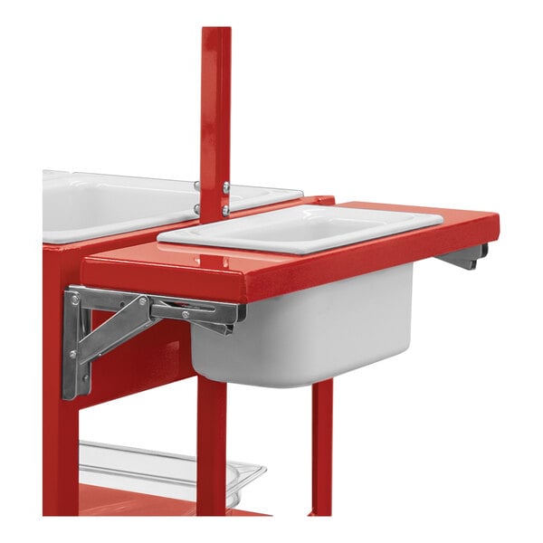 A red metal folding shelf with a white rectangular pan inserted, attached to a frame with metal brackets.