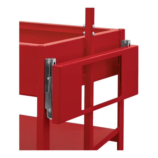 A partial view of a red metal cart or shelving unit with a foldable side shelf attached by metal hinges.